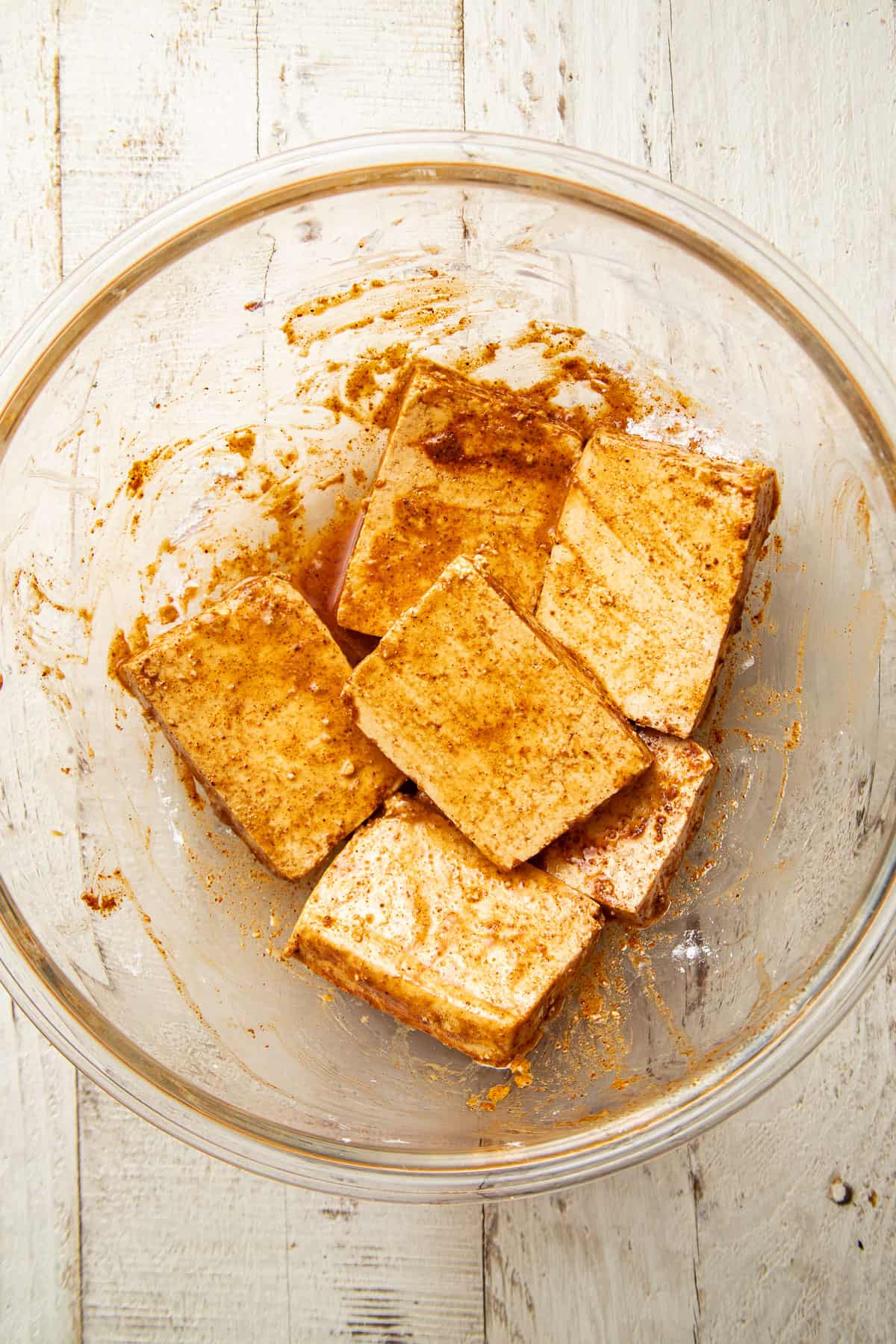 Tofu slices in a mixing bowl with oil, cornstarch, and spices.