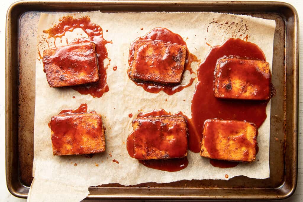 Baked tofu slices covered with barbecue sauce on a baking sheet.