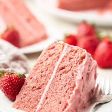 Vegan Strawberry Cake slices on a dish with cake and berries in the background.