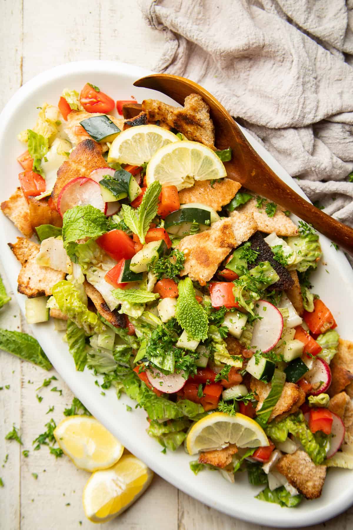 Dish of Fattoush Salad and serving spoon on a white wooden surface.
