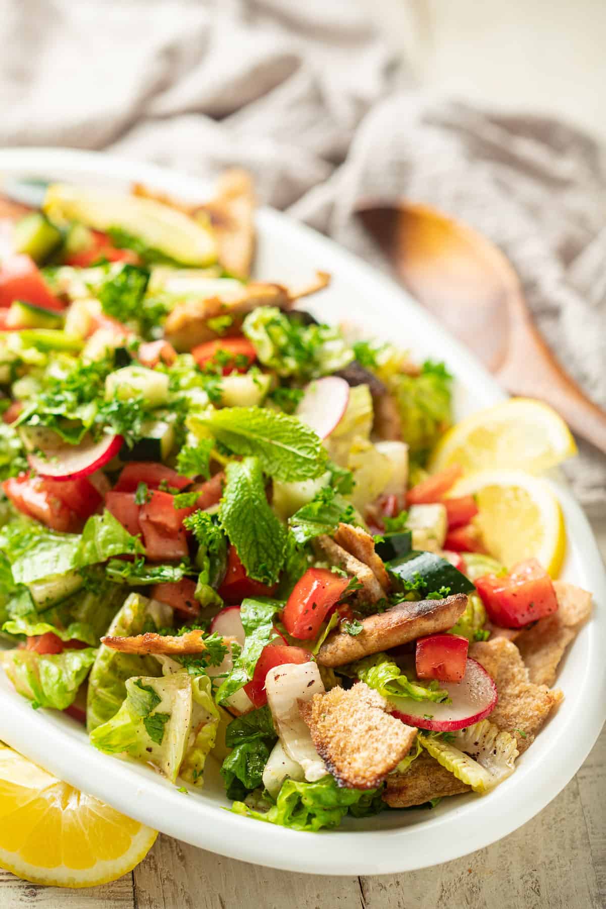 Close up of Fattoush Salad on a serving dish with lemon wedges.