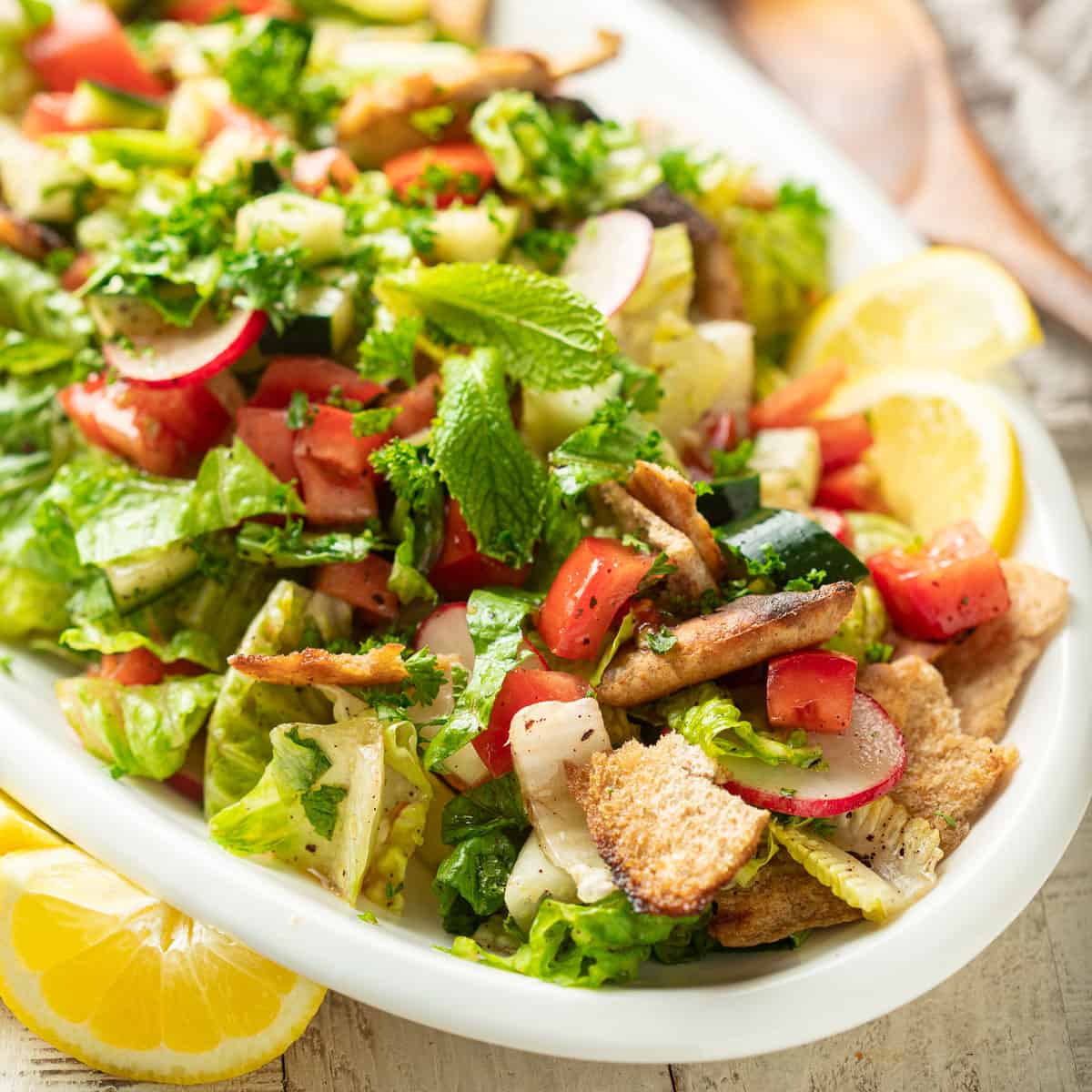 Close up of Fattoush Salad on a serving dish with lemon wedges.