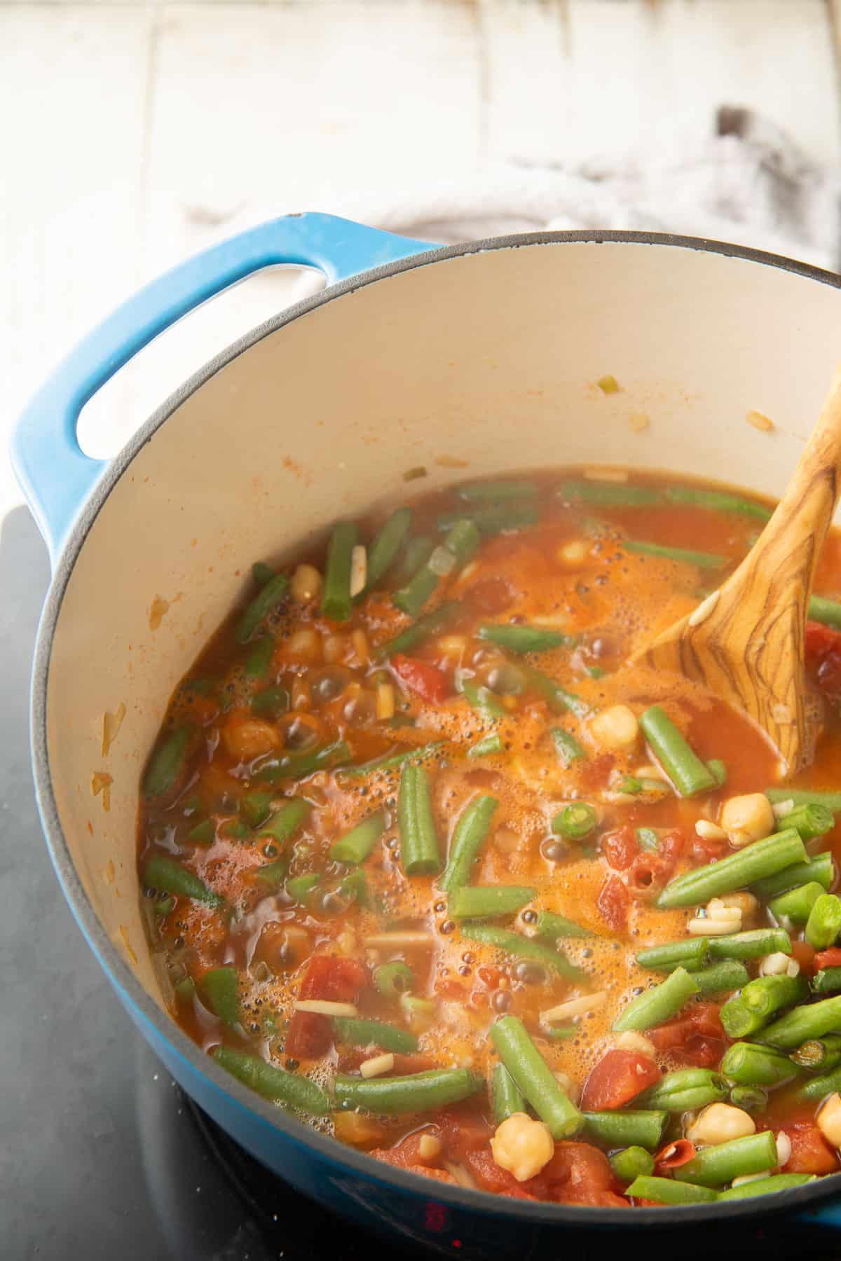 Green bean stew simmering in a pot with a wooden spoon.