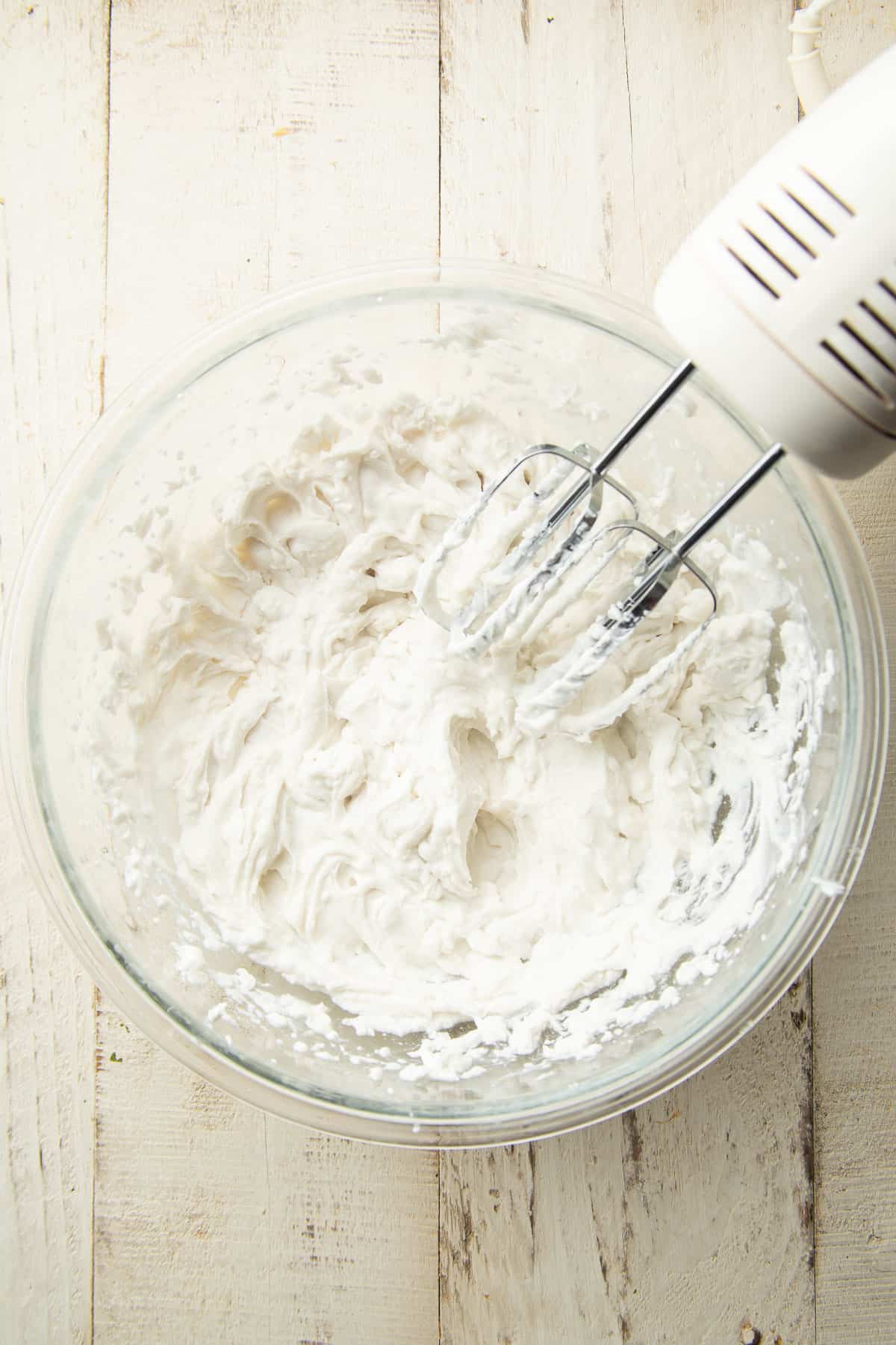 Coconut whipped cream in a mixing bowl with an electric mixer.