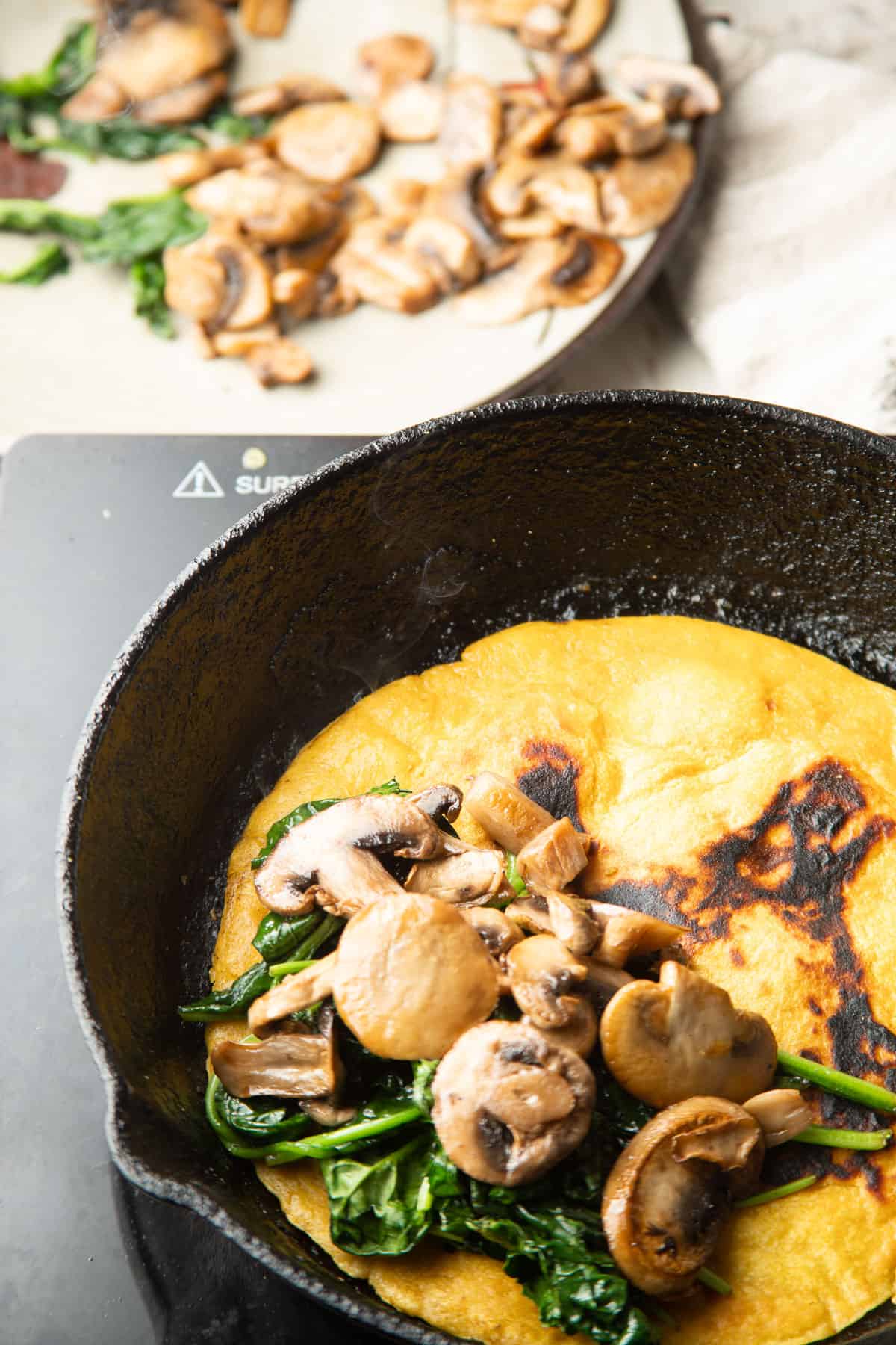 Vegan Omelet cooking in a skillet with mushrooms and spinach on top.