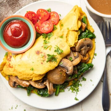 Vegan Omelet on a plate with a dish of ketchup and cherry tomatoes.