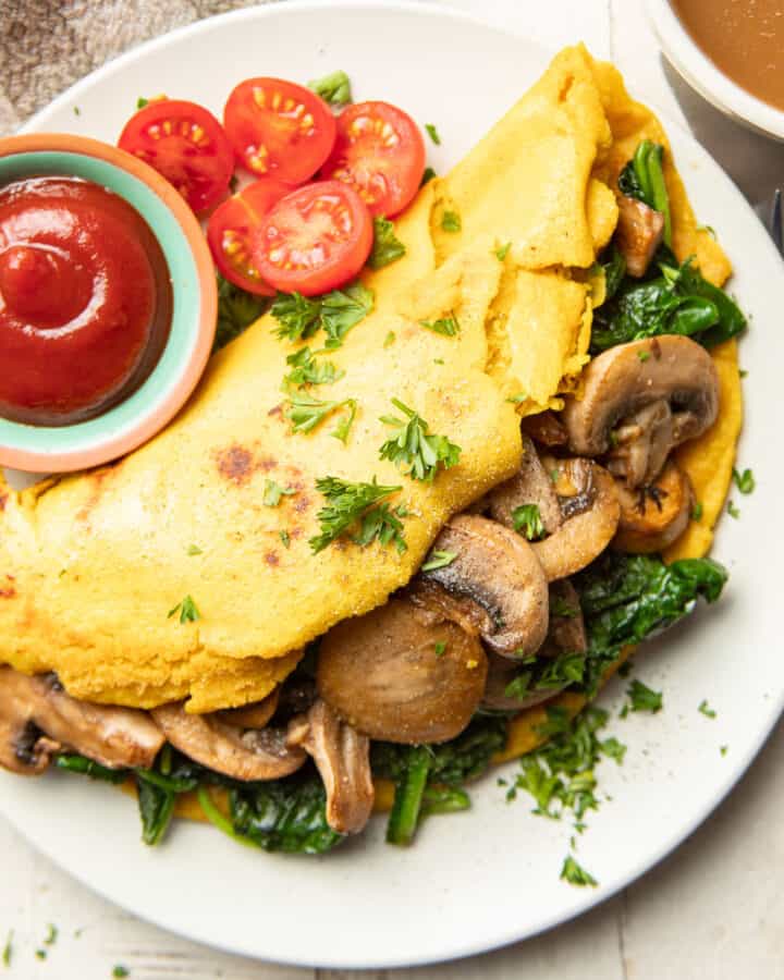 Vegan Omelet on a plate with a dish of ketchup and cherry tomatoes.