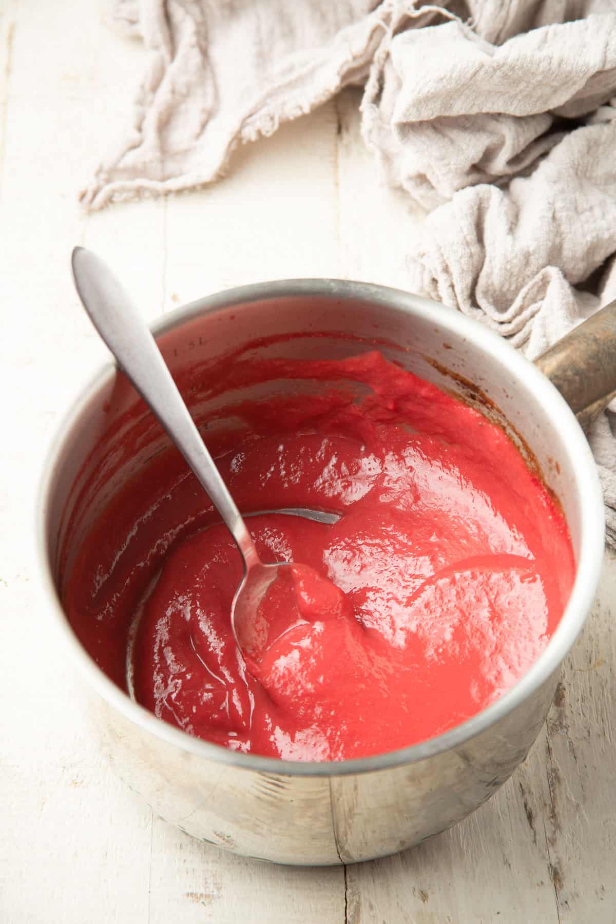 Reduced strawberry puree in a saucepan with spoon.