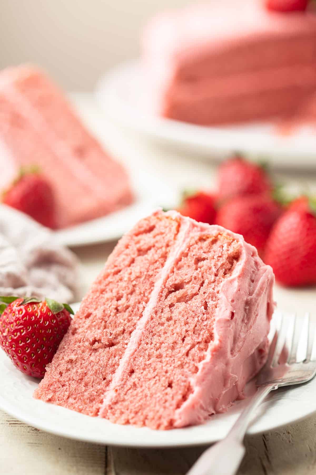 Vegan Strawberry Cake slices on a dish with cake and berries in the background.