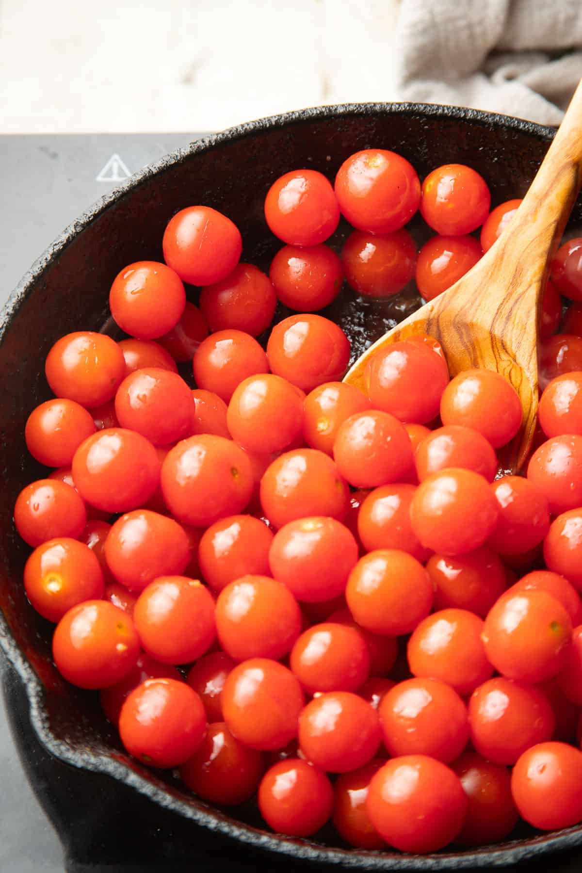 Cherry tomatoes in a skillet with a wooden spoon.