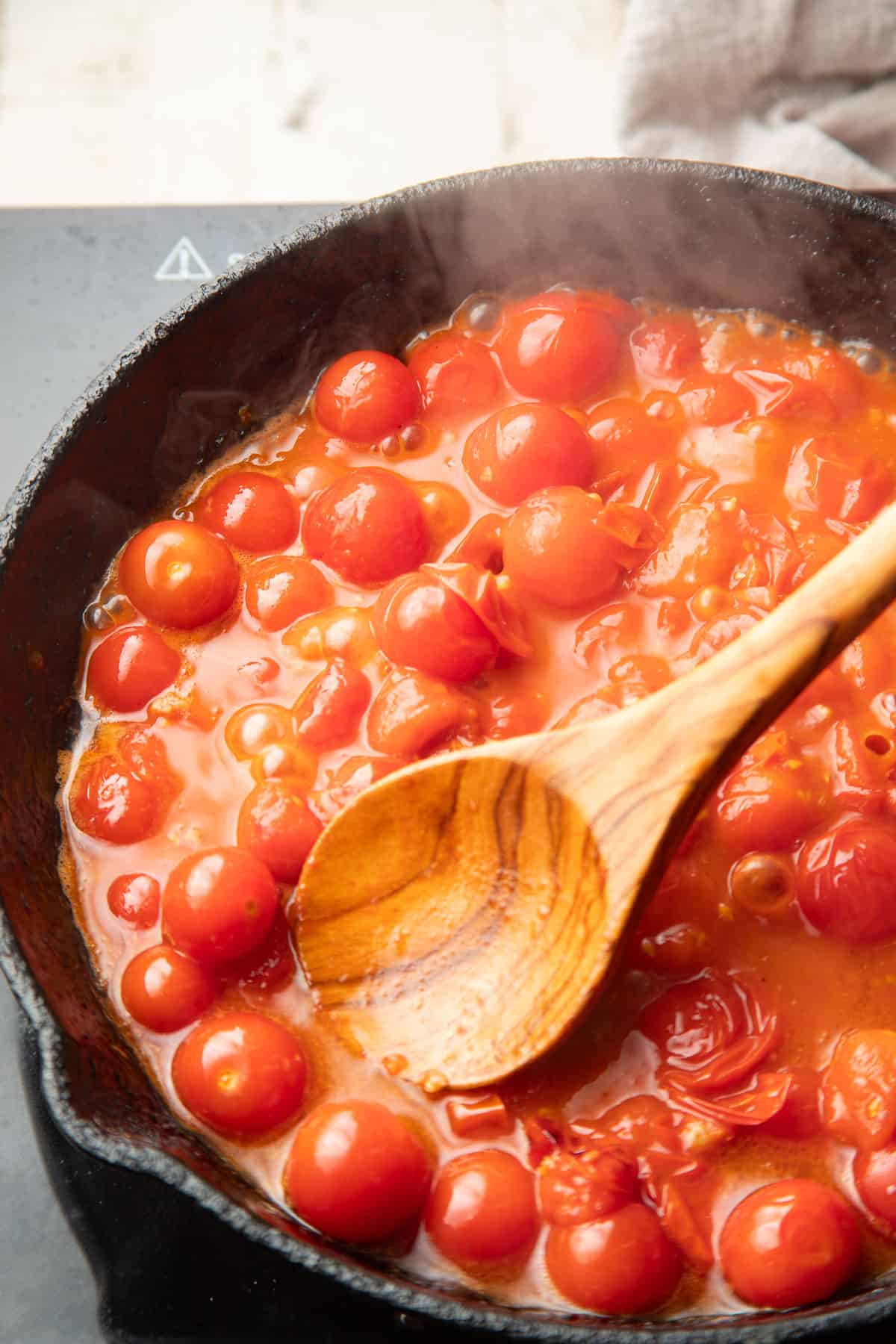 Cherry tomatoes cooking in a skillet with a wooden spoon.