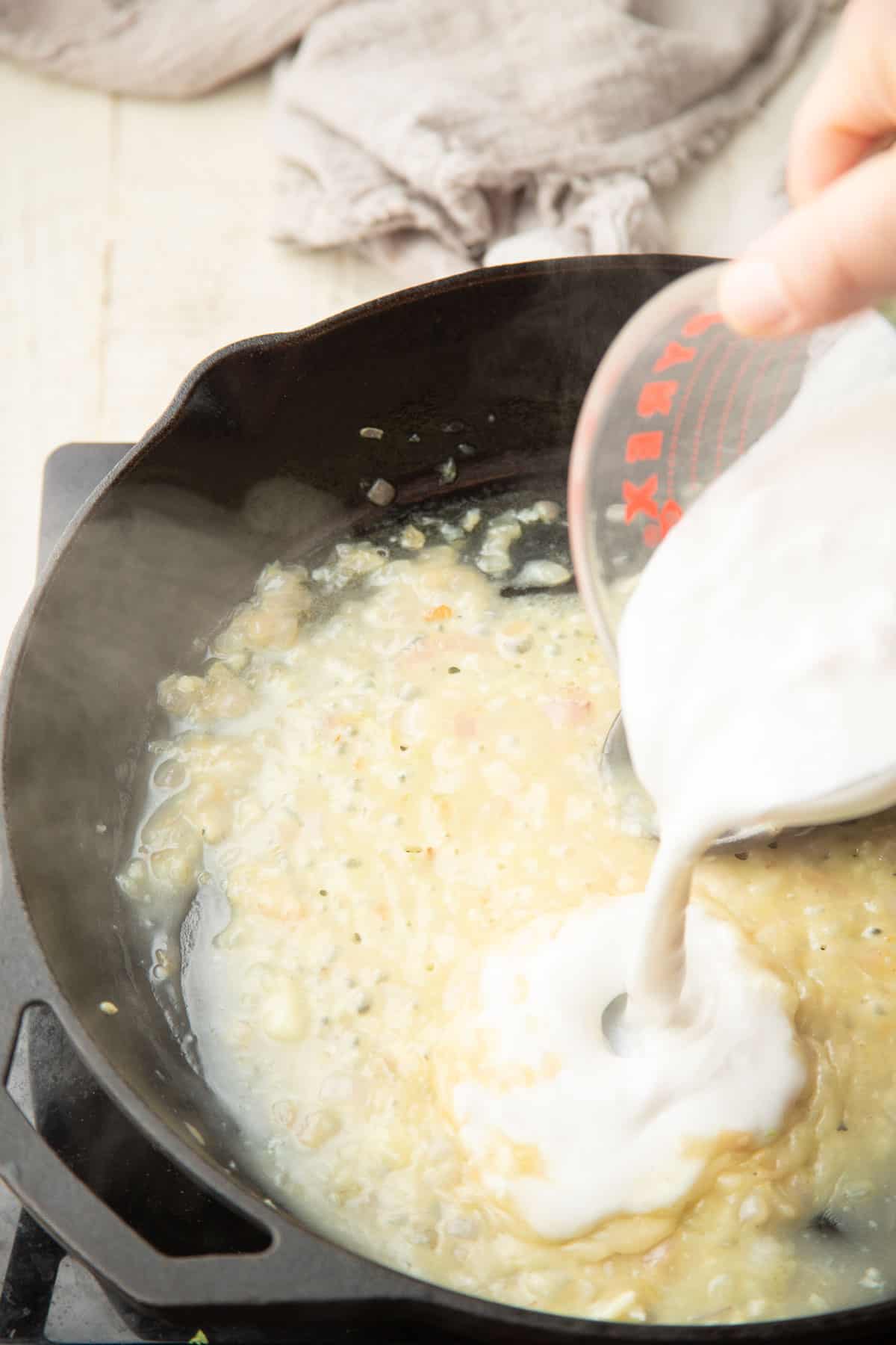 Coconut milk being poured into a skillet of shallots, white wine and flour.