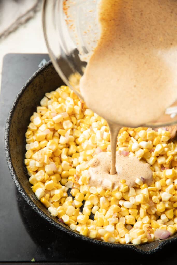 Sauce being poured into a skillet of corn cooking.