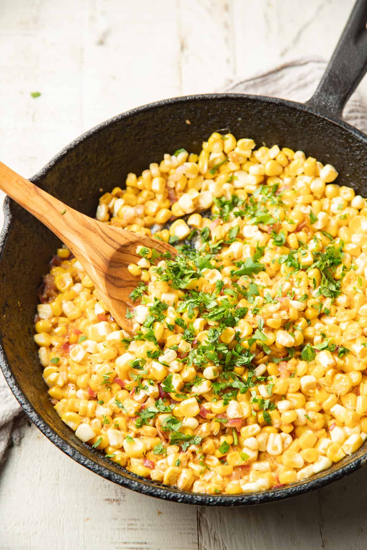 Street corn taco filling in a skillet with a wooden spoon.