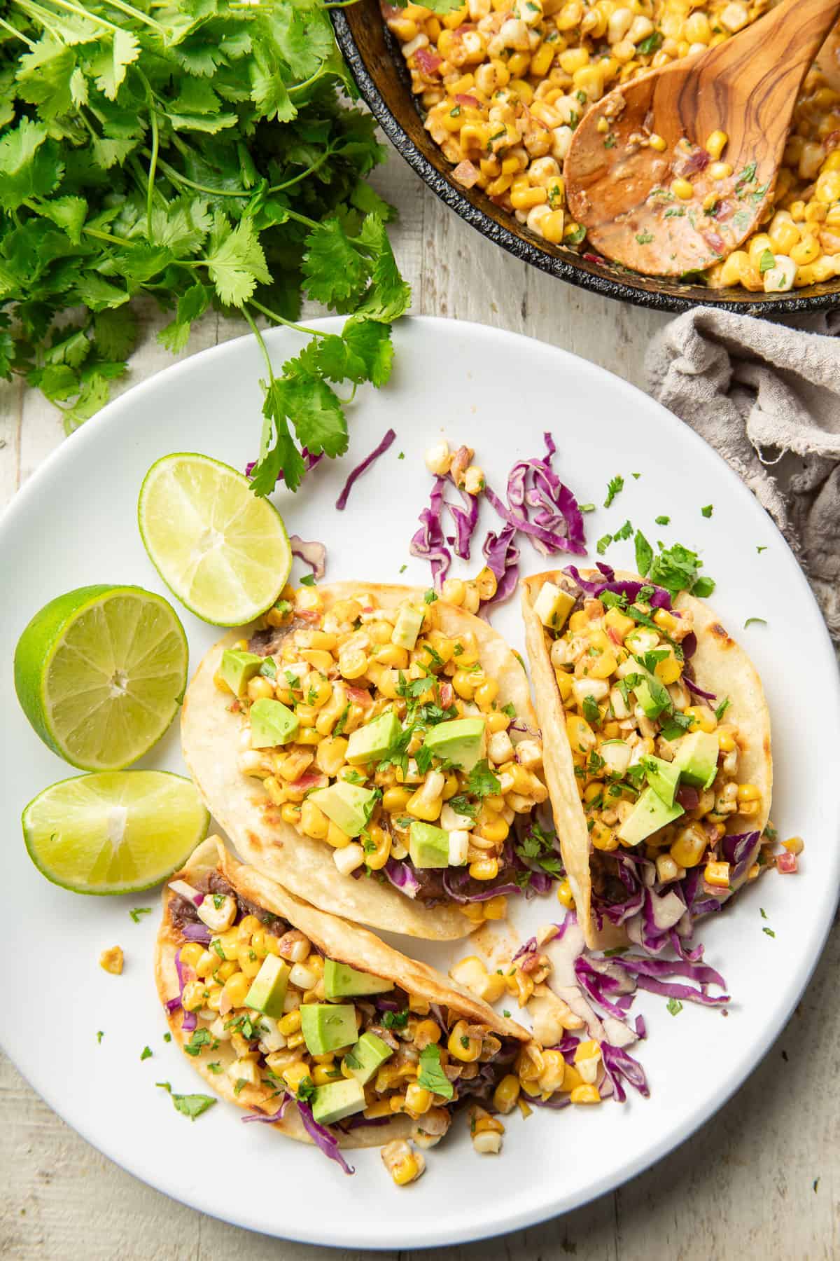 White wooden surface set with skillet, bunch of cilantro and plate of corn tacos.