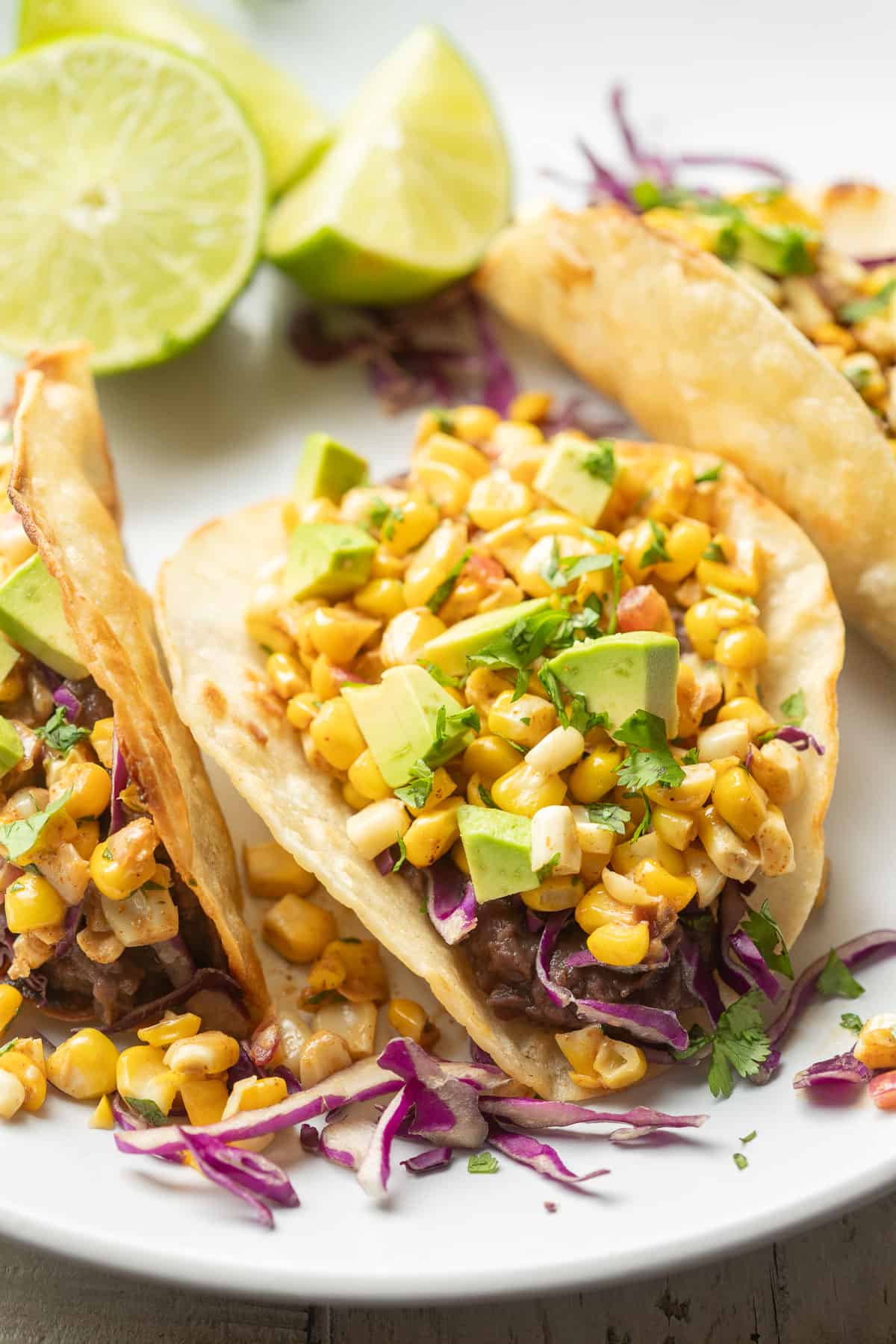 Close up of corn tacos on a plate with lime wedges in the background.