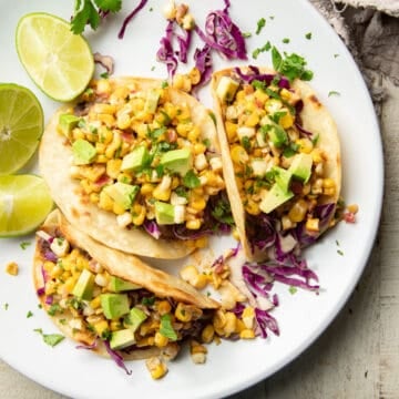 Three street corn tacos on a plate with lime wedges.