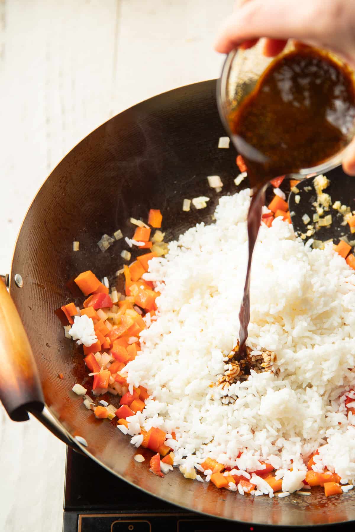 Hand pouring sauce into a skillet of veggies and rice.