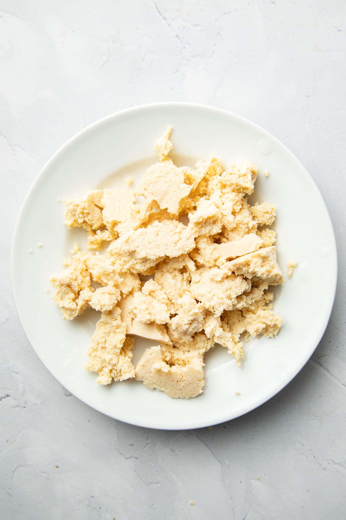 Crumbled super firm tofu that's been frozen and thawed on a plate.