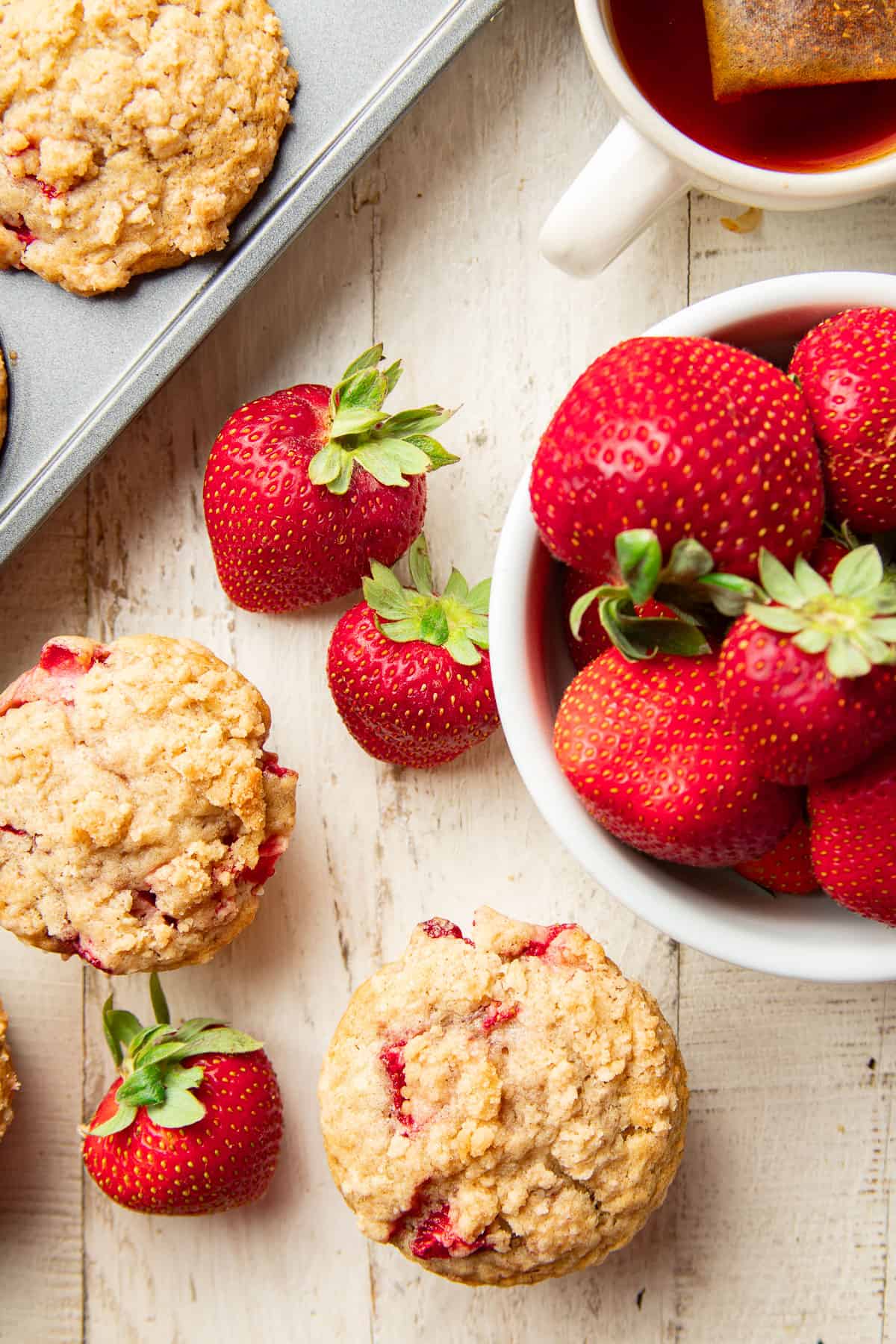 Vegan Strawberry Muffins and fresh strawberries on a white wooden surface.