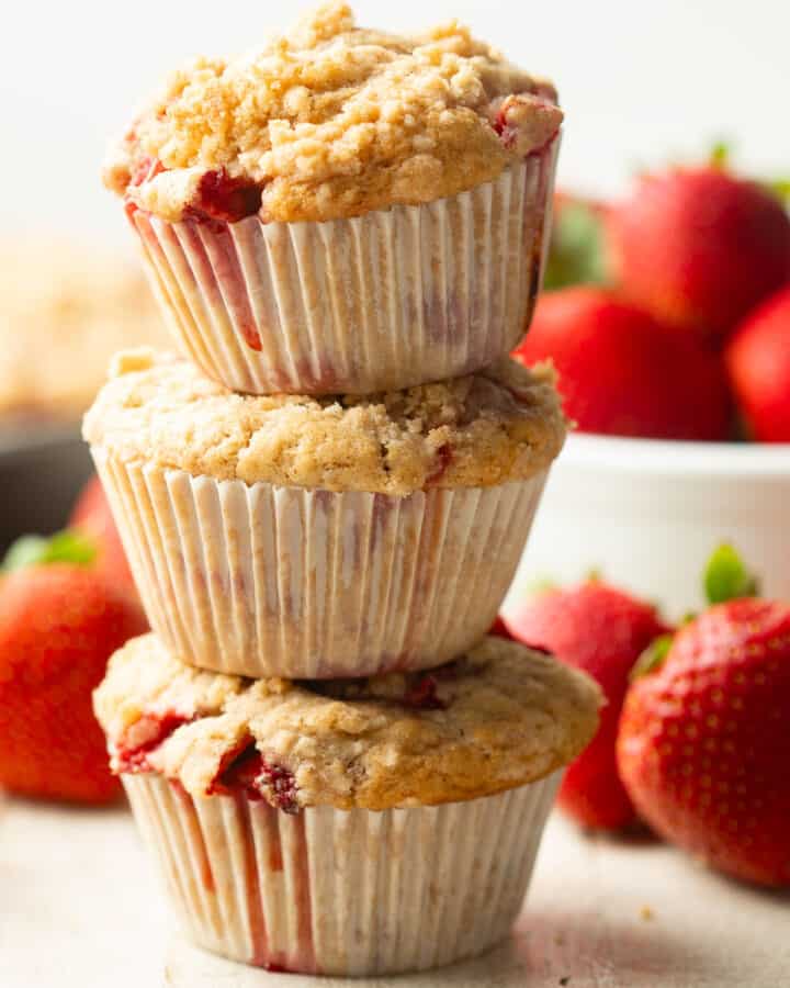 Stack of three Vegan Strawberry Muffins with fresh strawberries in the background.