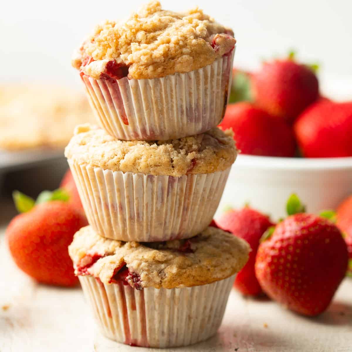 Stack of three Vegan Strawberry Muffins with fresh strawberries in the background.