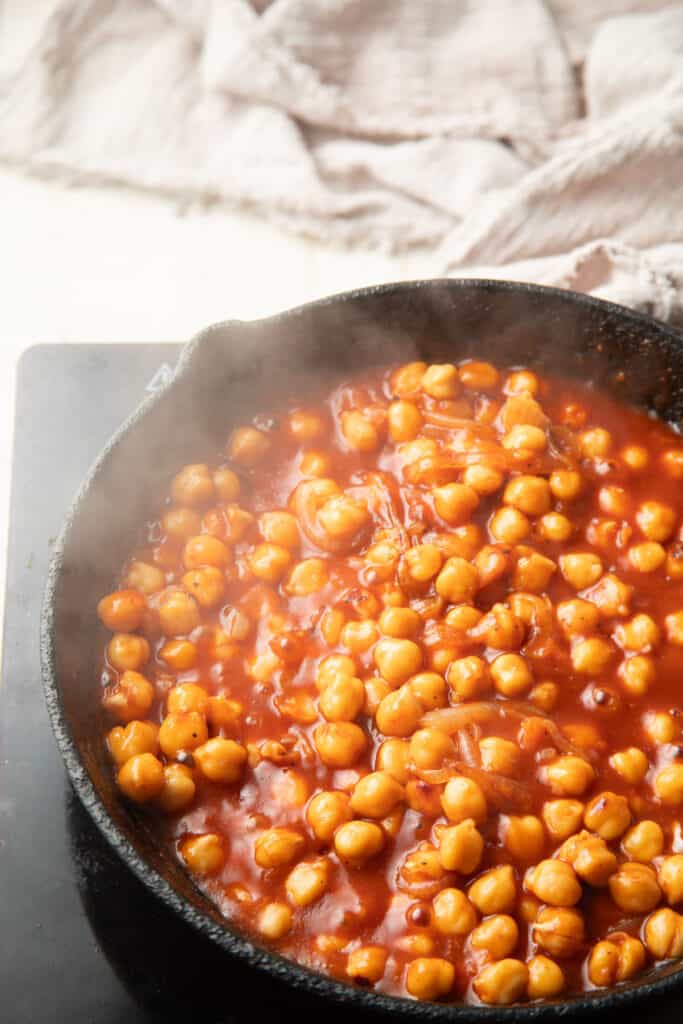 Chickpeas simmering in a skillet of barbecue sauce.