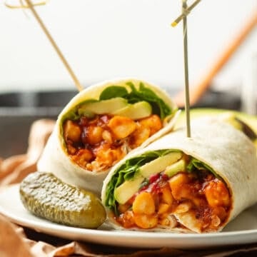 Two halves of a Barbecue Chickpea Wrap on a plate with a pickle.