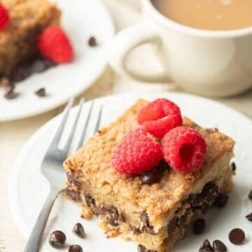 Slice of Vegan Chocolate Chip Crumb Cake with raspberries on top, coffee cup in the background.