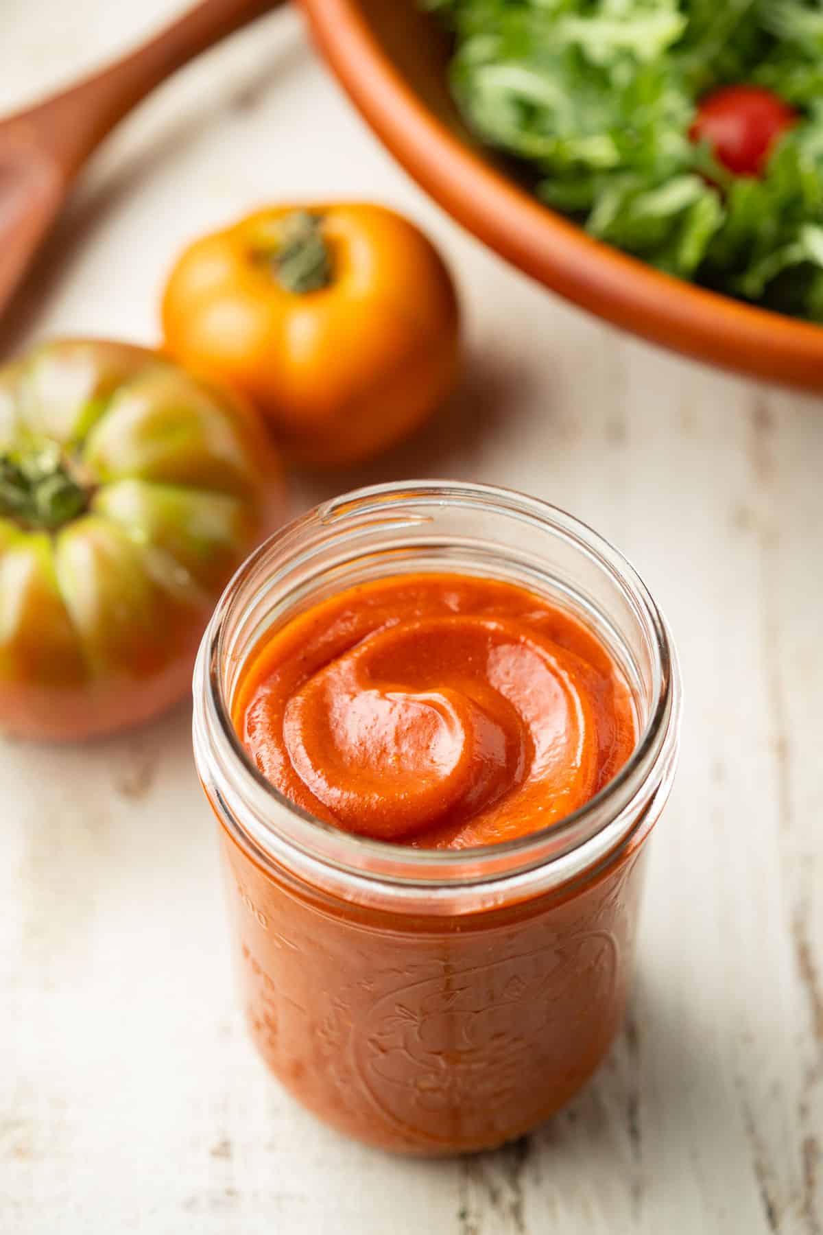 Jar of Vegan French Dressing with tomatoes and salad bowl in the background.