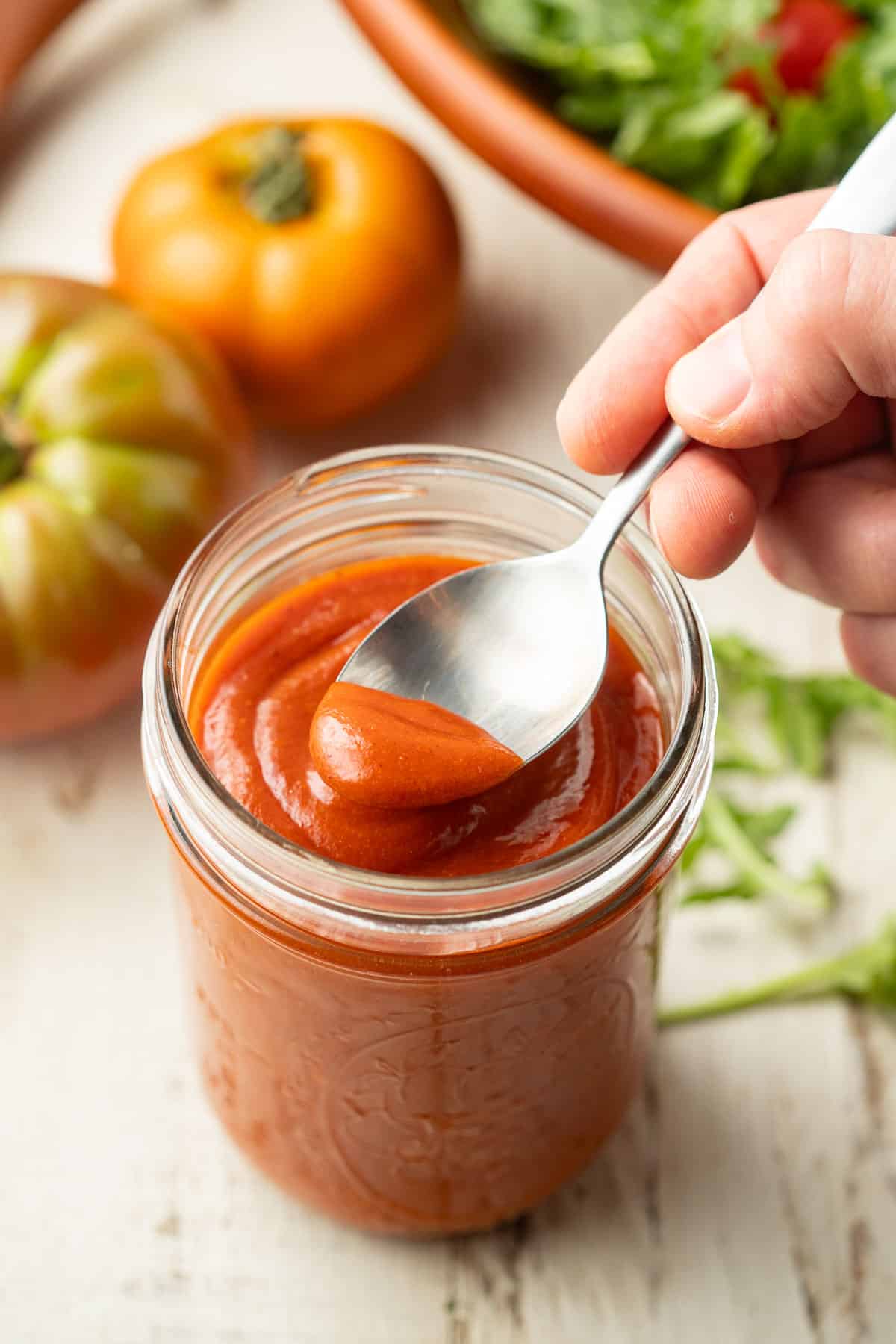 Hand dipping a spoon into a jar of Vegan French Dressing.