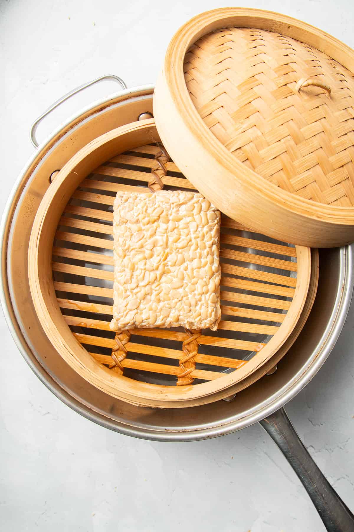 Block of tempeh in a bamboo steamer in a wok.