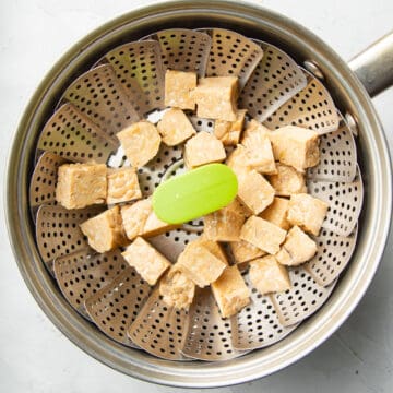 Diced tempeh in a steamer basket in a saucepan.