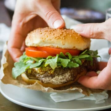 Pair of hands holding a portobello mushroom burger over a plate.