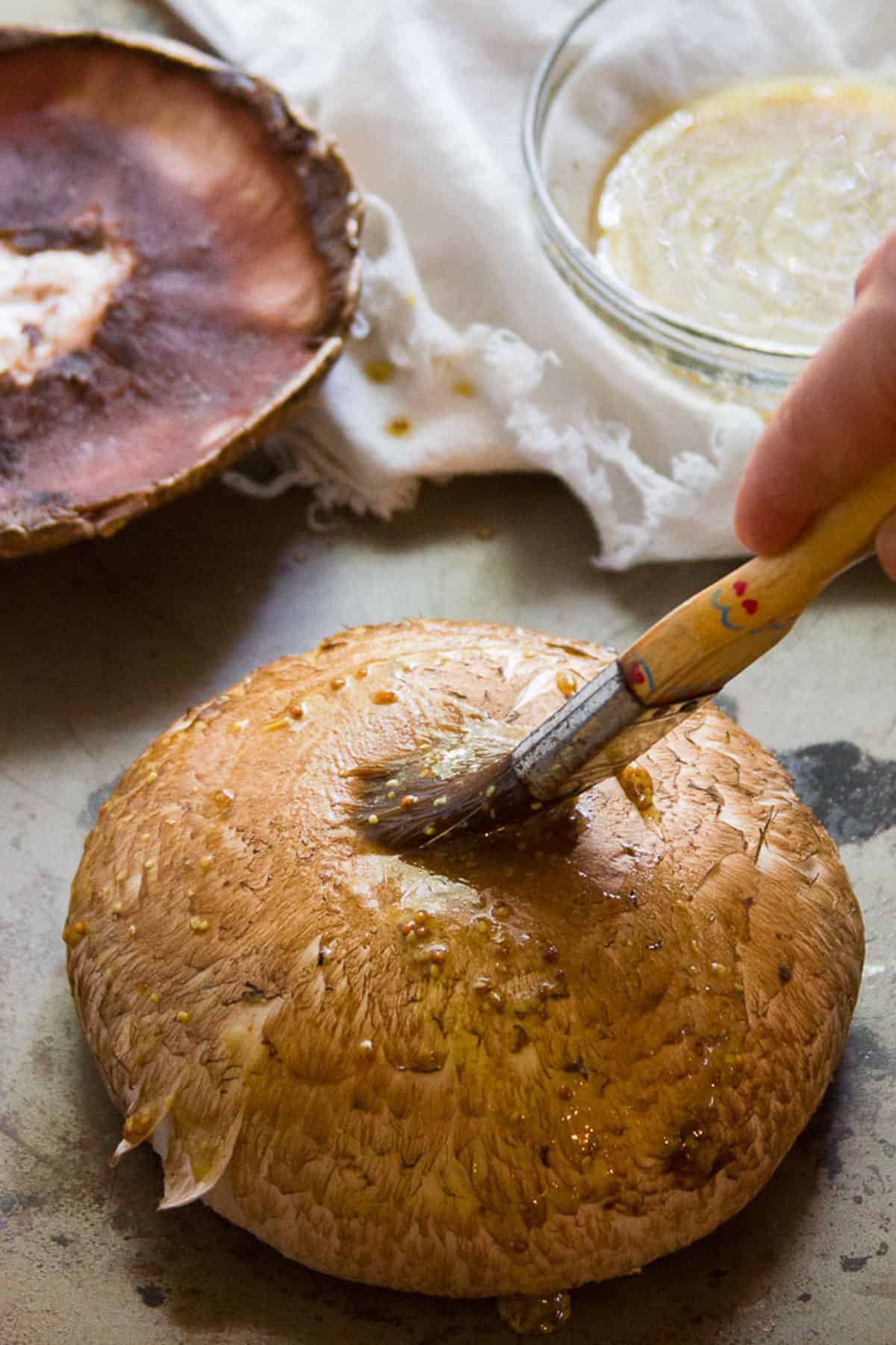 Sauce being brushed on a portobello mushroom cap.