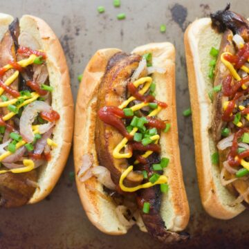 Three portobello hot dogs with ketchup, mustard, scallions and onions on top.