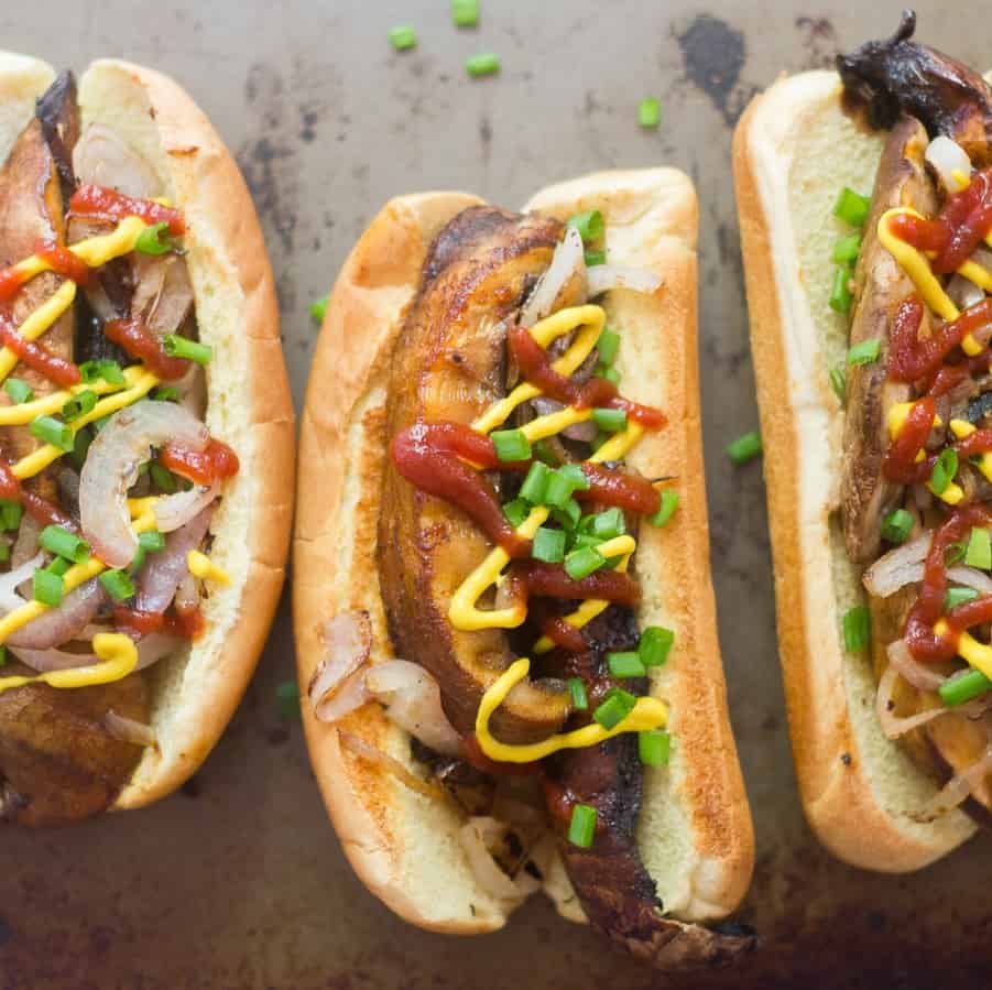 Three portobello hot dogs with ketchup, mustard, scallions and onions on top.