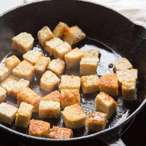 Tempeh cubes pan-frying in a skillet.
