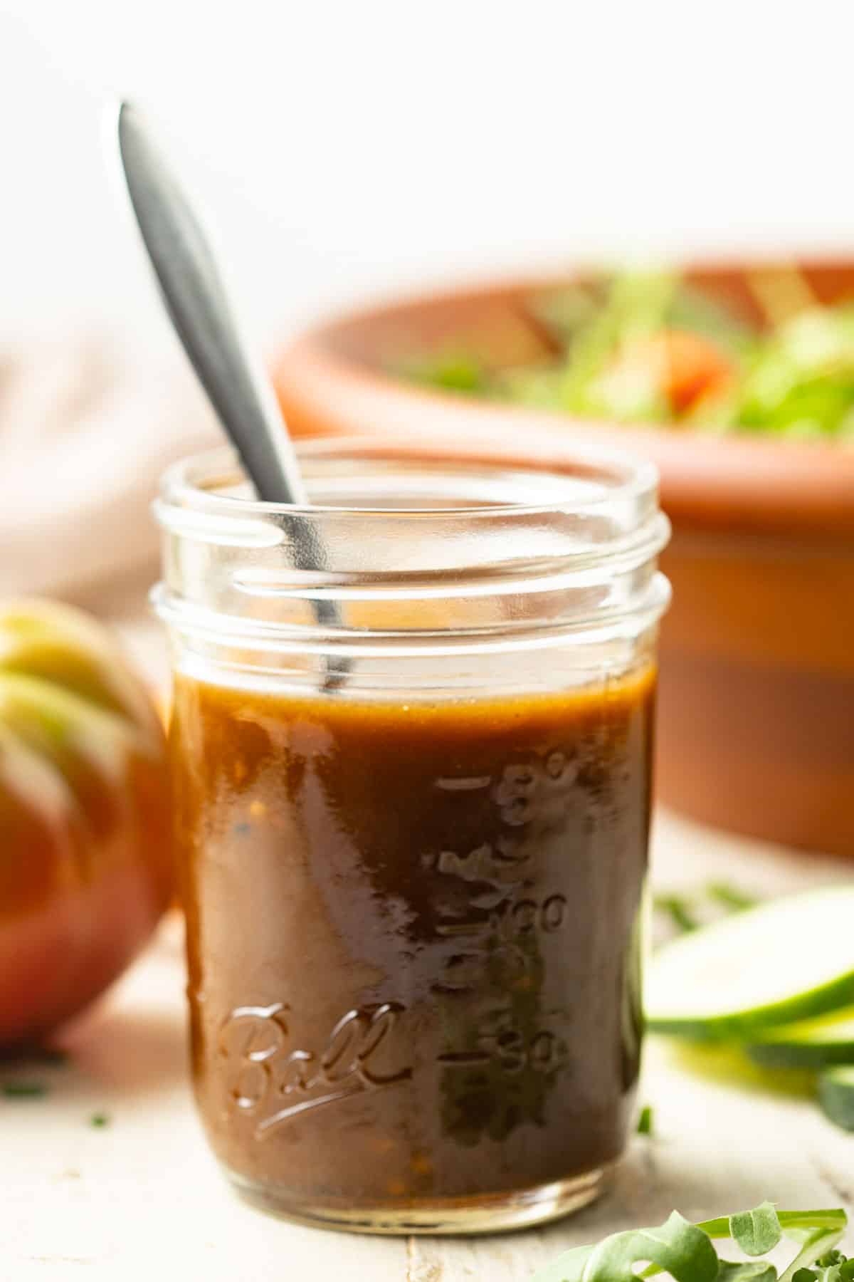 jar of Maple Balsamic Vinaigrette with salad bowl and vegetables in the background.