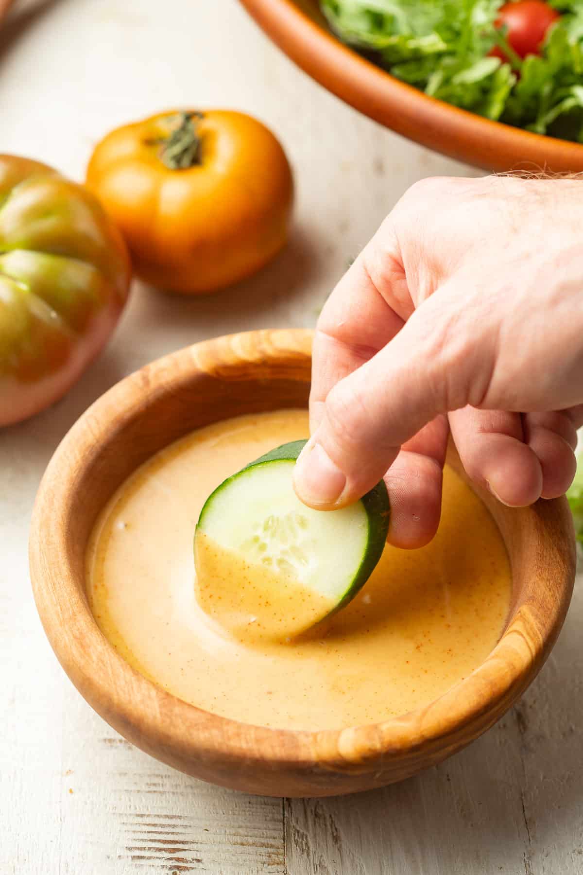 Hand dipping a cucumber slice into a bowl of Vegan Honey Mustard.