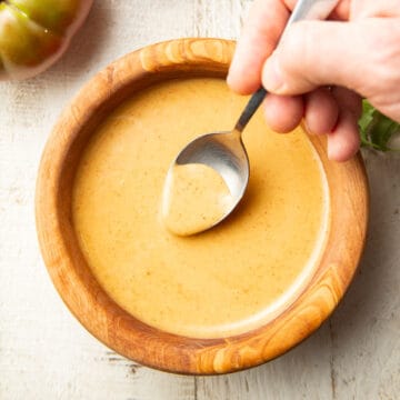 Hand dipping a spoon into a bowl of Vegan Honey Mustard sauce.