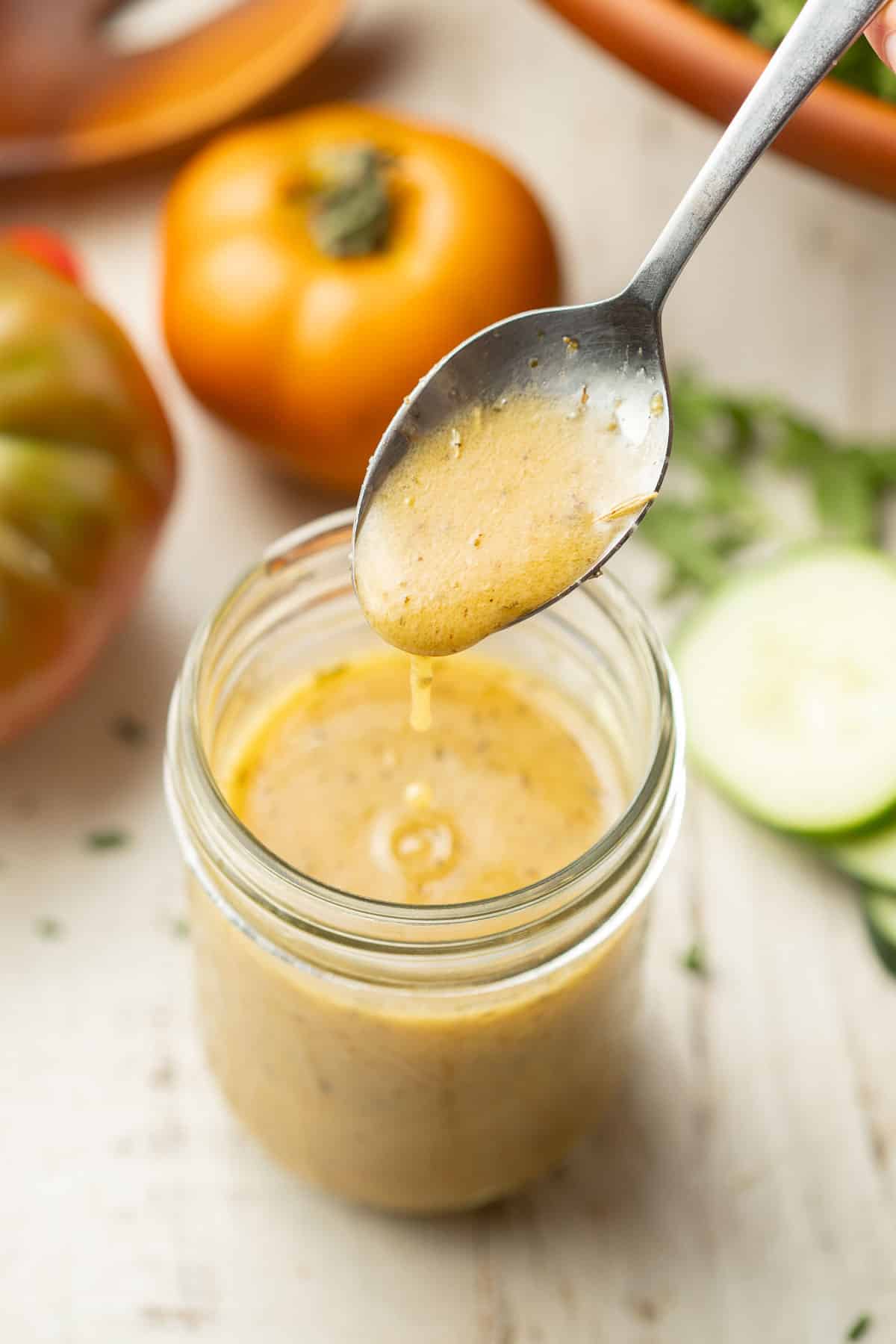 Spoon drizzling Vegan Italian Dressing into a jar.