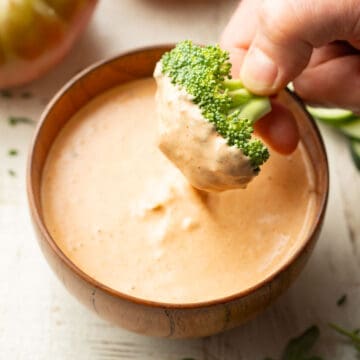 Hand dipping a broccoli floret into a bowl of Vegan Russian Dressing.
