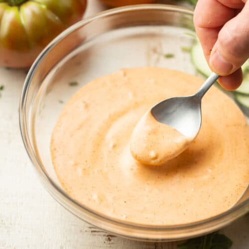 Hand dipping a spoon into a bowl of Vegan Thousand Island Dressing.