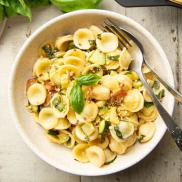 Bowl of Pasta with Zucchini and Roasted Garlic with fork and spoon.