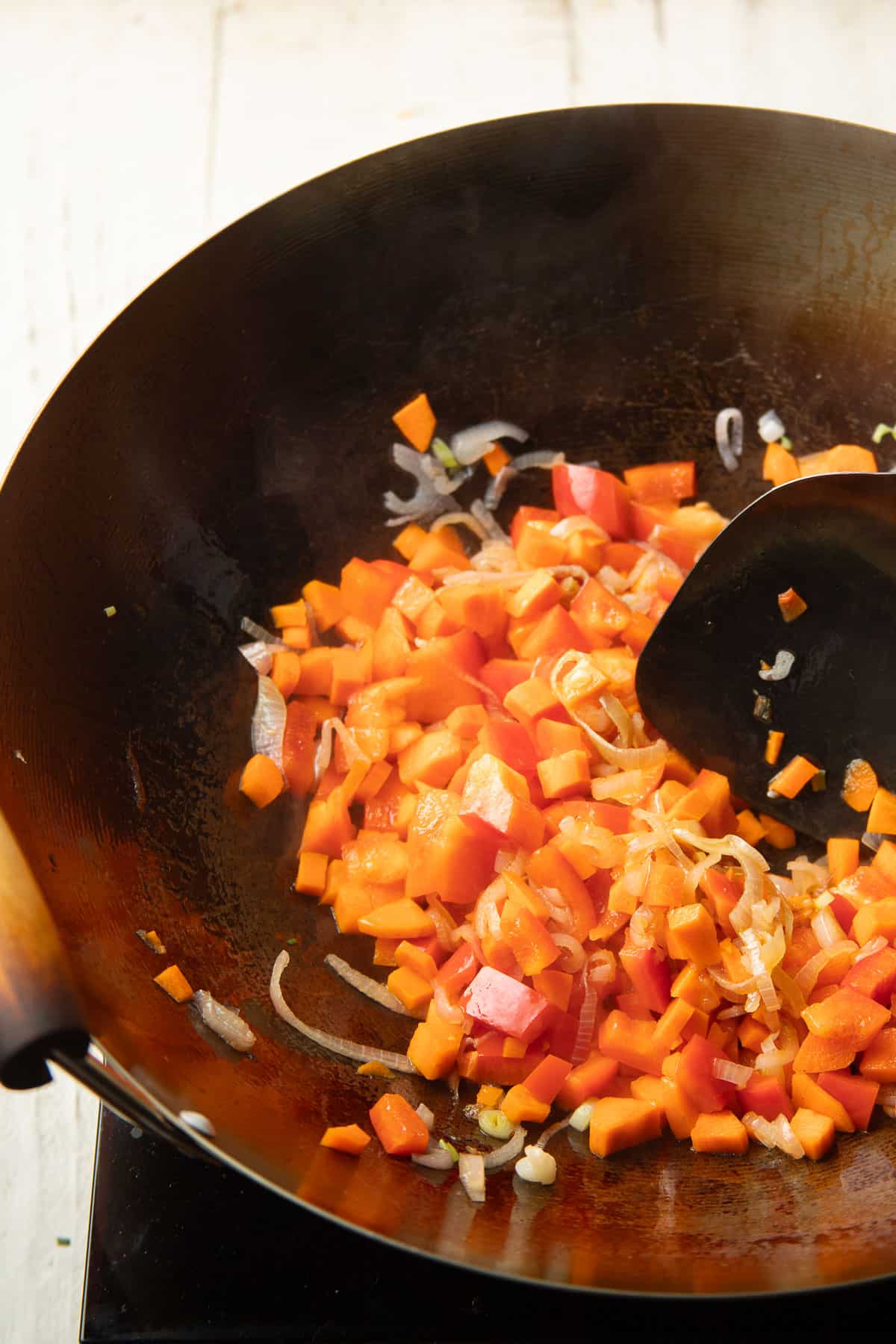 Carrots, bell pepper, and shallots being stir-fried in a wok.