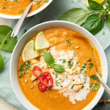 Two bowls of Thai Pumpkin Soup with basil and lime wedges on the side.