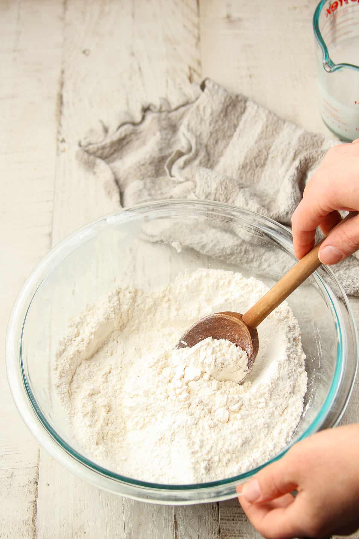 Hand stirring dry ingredients for biscuit dough together in a glass bowl.