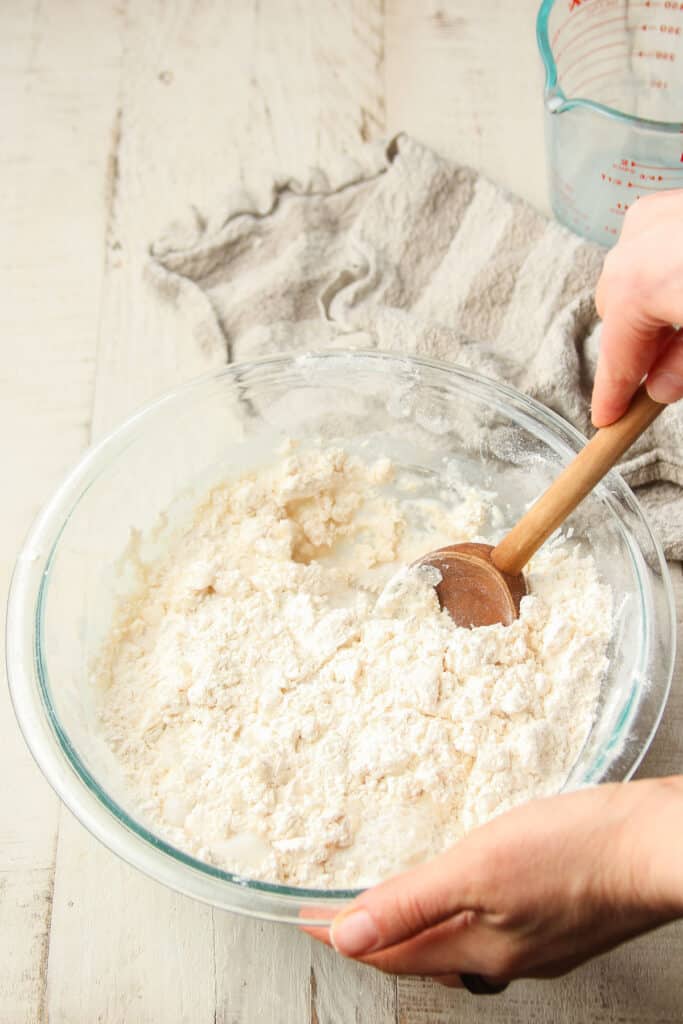 Hand stirring vegan biscuit dough together in a mixing bowl.