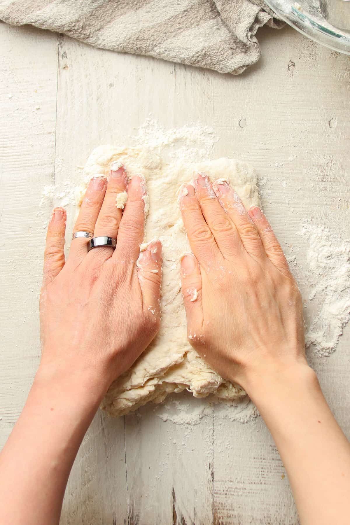 Hands flattening a square of biscuit dough.